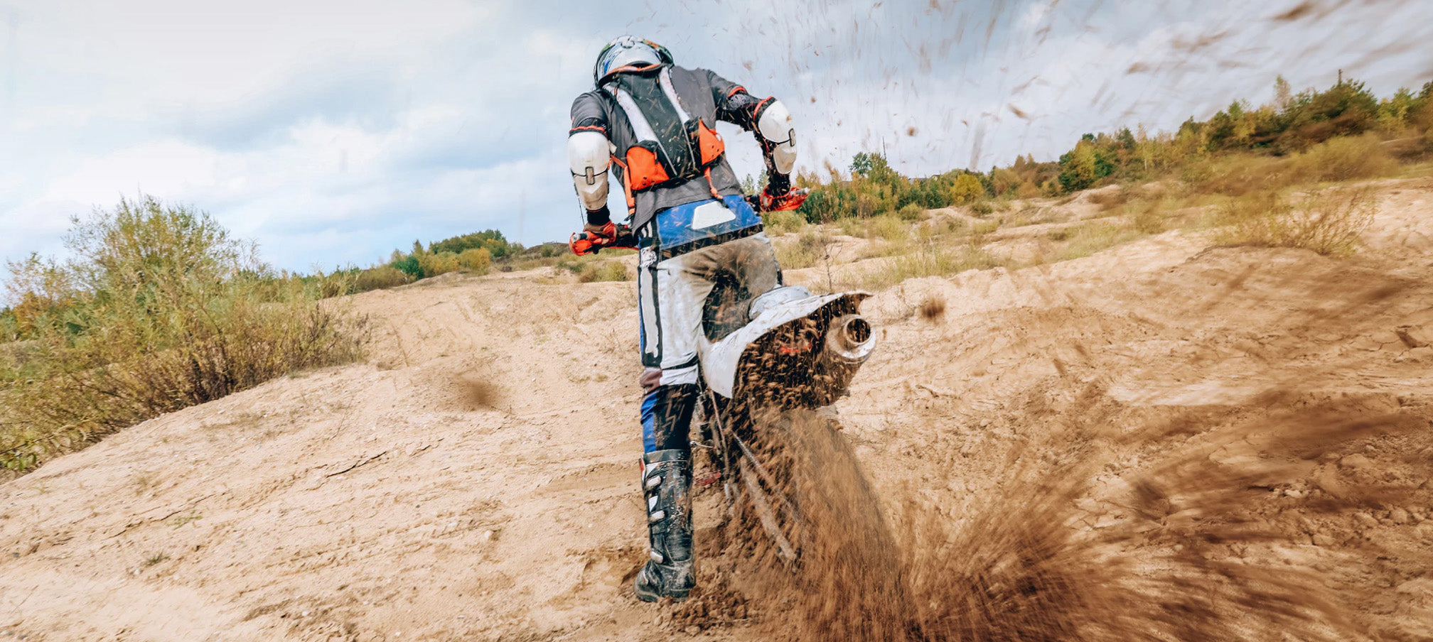 Dirt bike rider spinning tires in the mud, flinging dirt up towards the camera