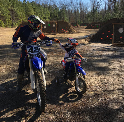 Our Expert, Brian, fist-bumping his young son while both pose on blue dirt bikes