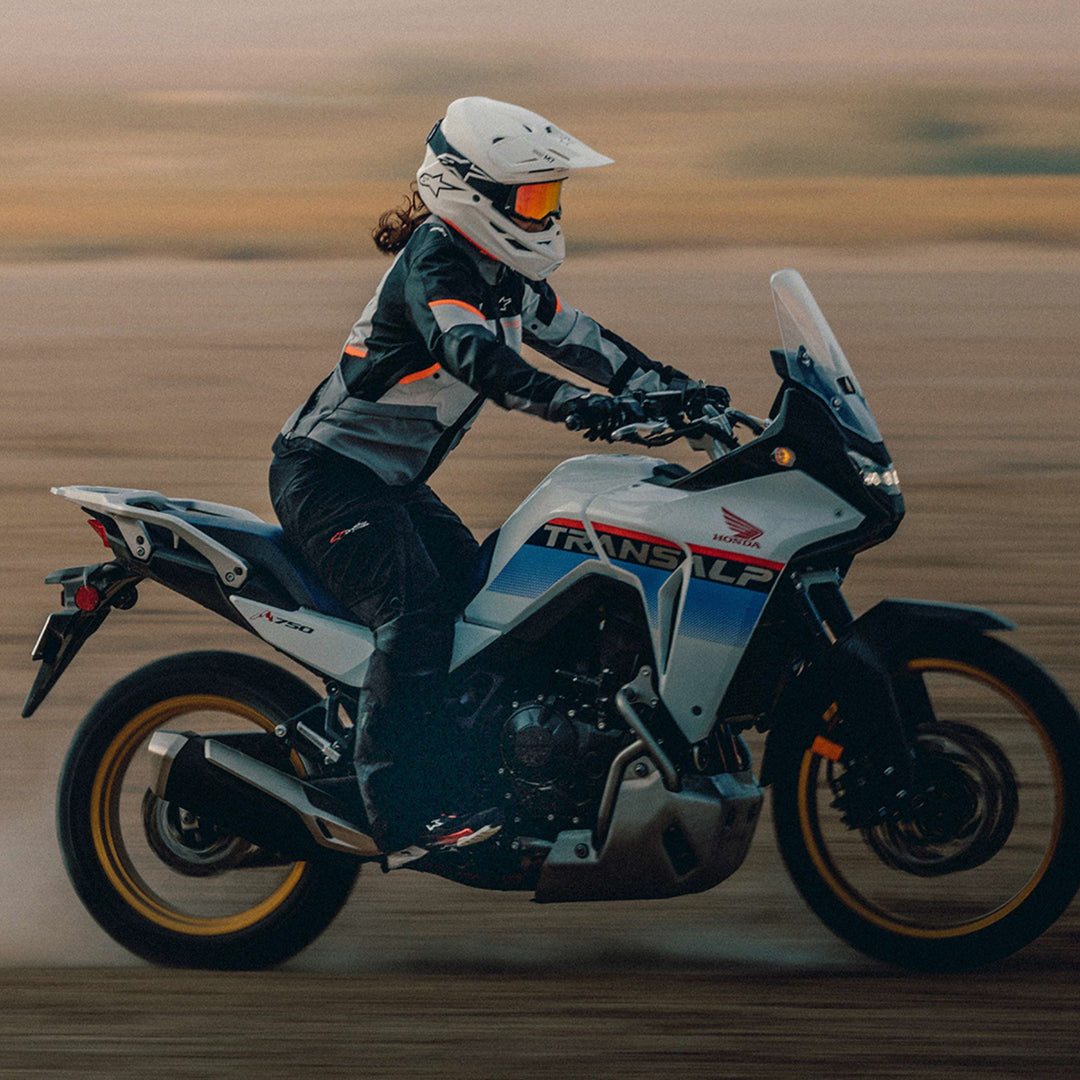 Alpinestars Stella Andes V4 Drystar Jacket Dark Gray/Ice Gray Black/Coral - Lifestyle Side Shot of Rider Wearing Jacket While Riding Through Desert on White Adventure Motorcycle