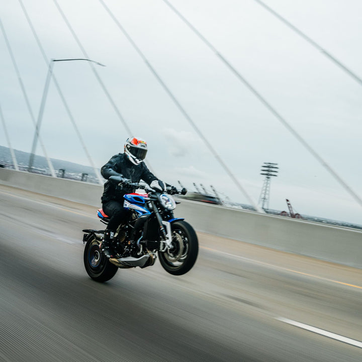 Cortech Men's Hyper-Tec 2.0 Jacket Black/White - Lifestyle shot of rider in jacket doing wheelie with blue motorcycle on bridge