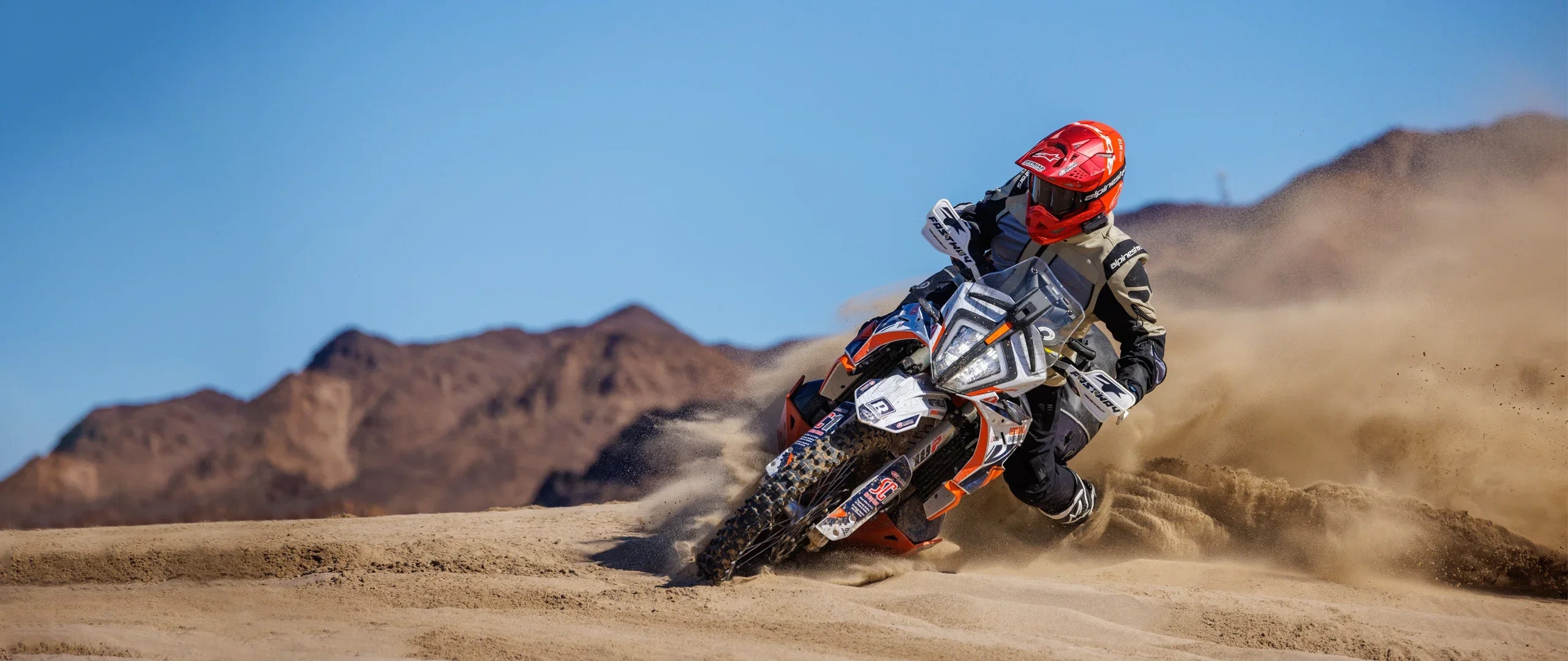 Adventure rider sliding through sand, while wearing helmet with Cardo Packtalk Edge installed