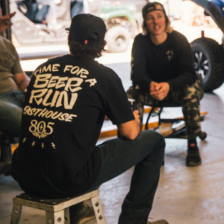 Fasthouse 805 Beer Run Tee Black - Lifestyle shot of man wearing shirt sitting on bike stand in garage
