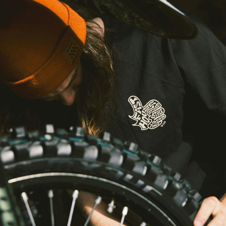 Fasthouse Satisfaction SS Tee Black - Lifestyle Close-Up of Person Wearing Shirt while Checking Tire