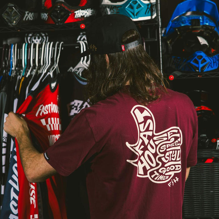 Fasthouse Satisfaction SS Tee Maroon - Lifestyle Rear View of Person Wearing Shirt while looking through rack of Fasthouse Jerseys