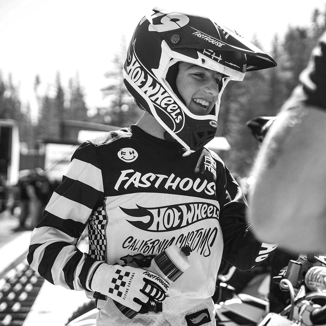 Fasthouse Youth Grindhouse Hot Wheels Jersey White/Black - Lifestyle Shot of Rider Wearing Jersey at Track Sideline