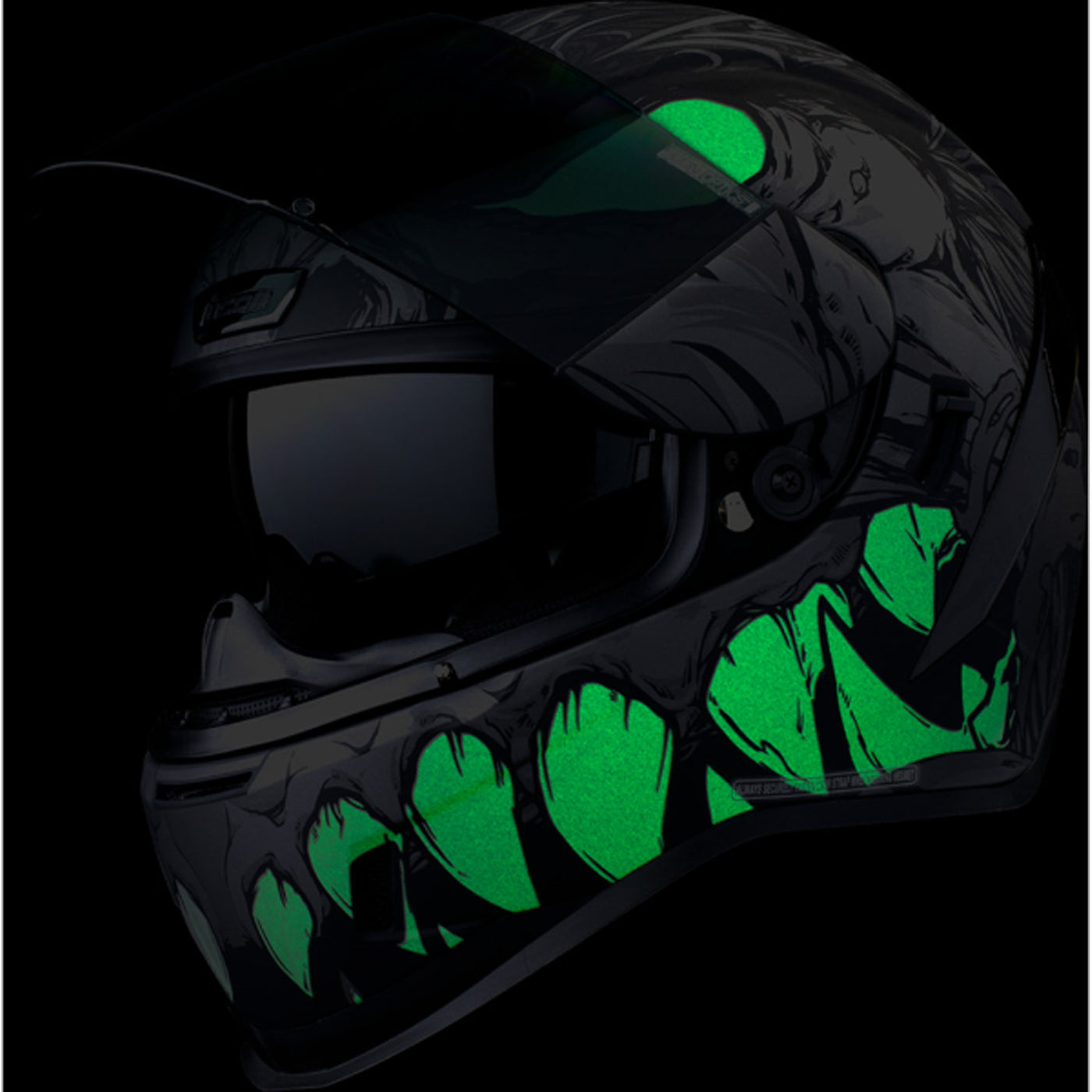 ICON Airform Manik'RR MIPS Helmet Dark Black - Front Left Side View with Dark Studio Background, Glow-in-the-Dark Graphics, Faceshield Raised, and Drop Down Sun Visor Lowered