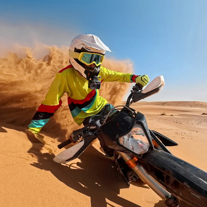 Insta360 Ace Pro 2 Motorcycle Bundle - Lifestyle Action Shot of Dirt Bike Rider Turning in Desert with Sand Cloud Trailing Behind, with Camera Mounted to Mouth Vent of Helmet