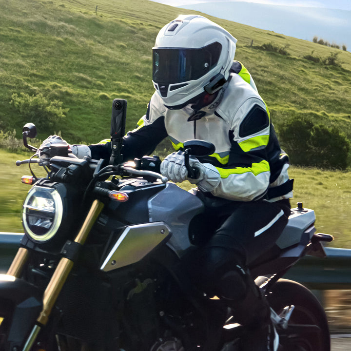 Insta360 X5 Motorcycle Bundle - Lifestyle Shot of Motorcycle Rider Speeding Past Fields with X5 Camera Attached to Fork Stem Mount