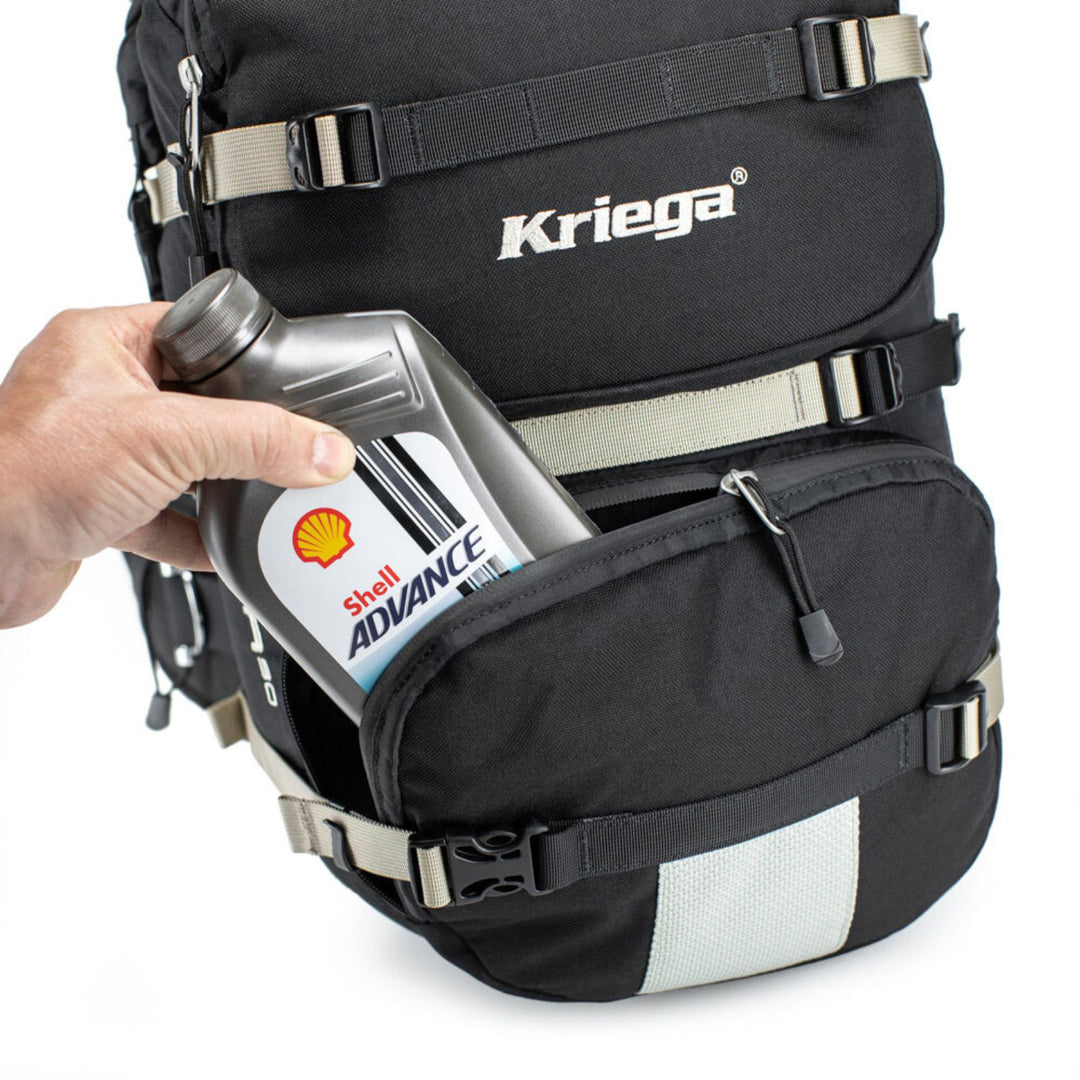 Kriega R30 Backpack - Close-Up of Model Placing Oil Bottle into Lower Front Zippered Pocket