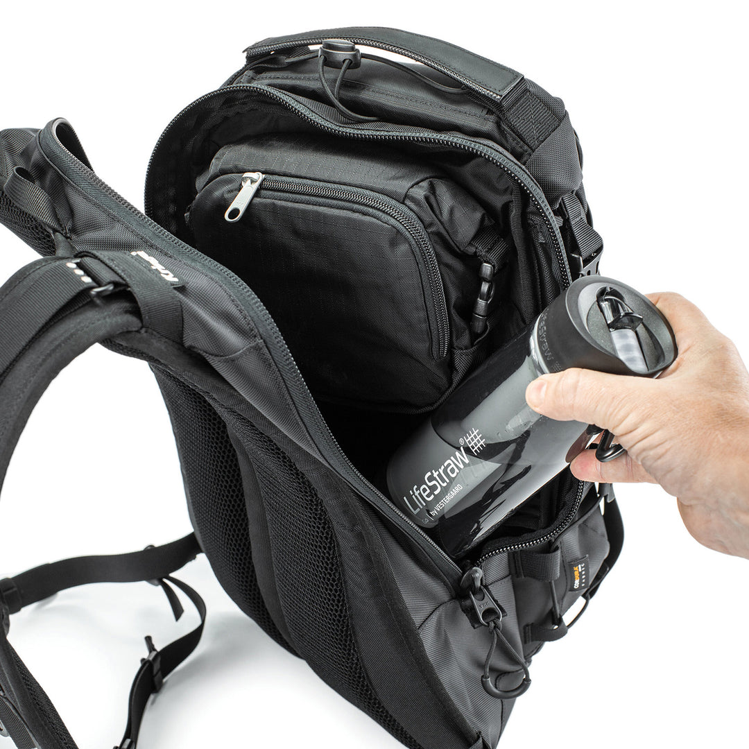 Kriega Trail 18 Adventure Backpack Black - Close-Up of Model Placing Water Bottle into Mid Section