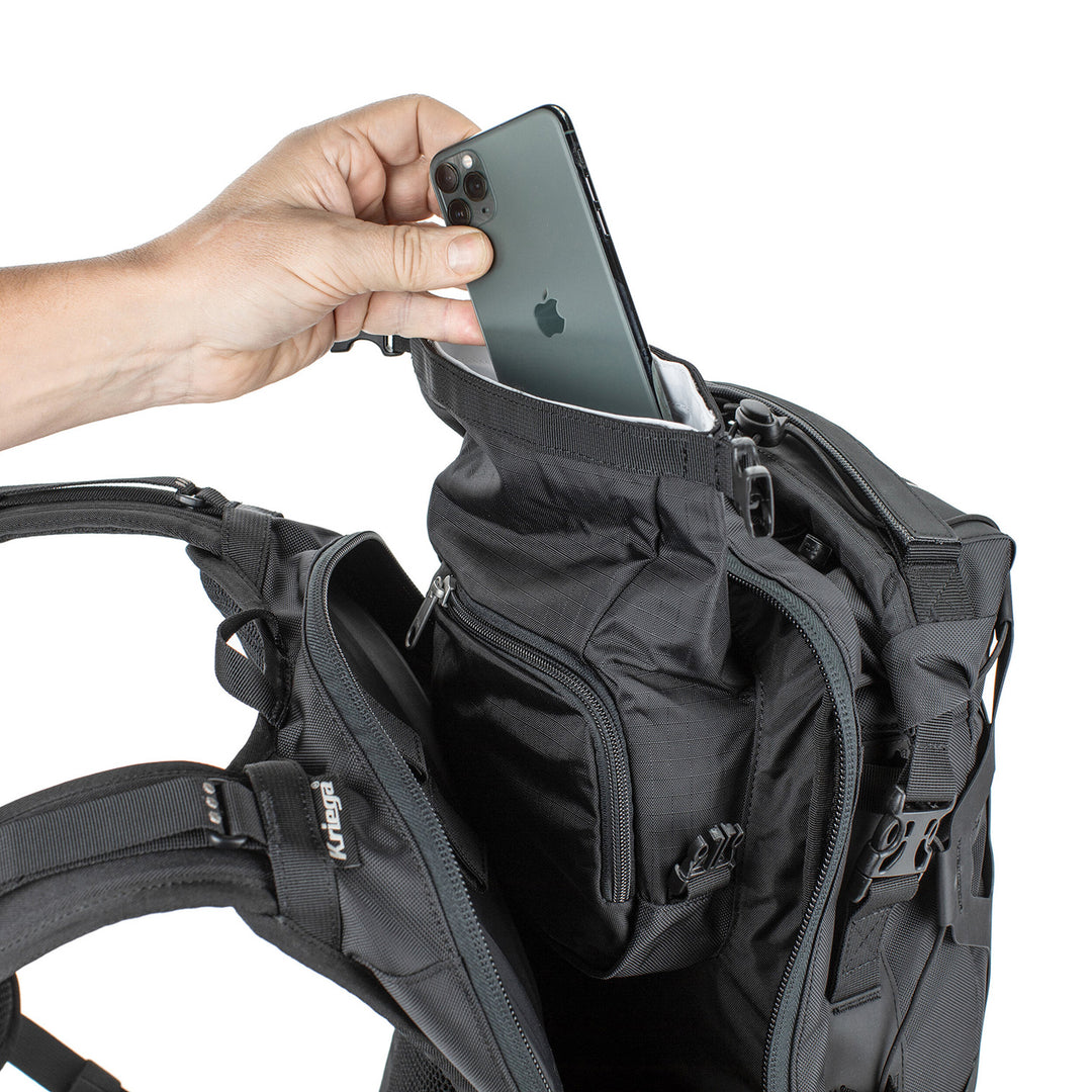 Kriega Trail 18 Adventure Backpack Black - Close-Up of Model Placing Phone into Top of Mid Section Pocket