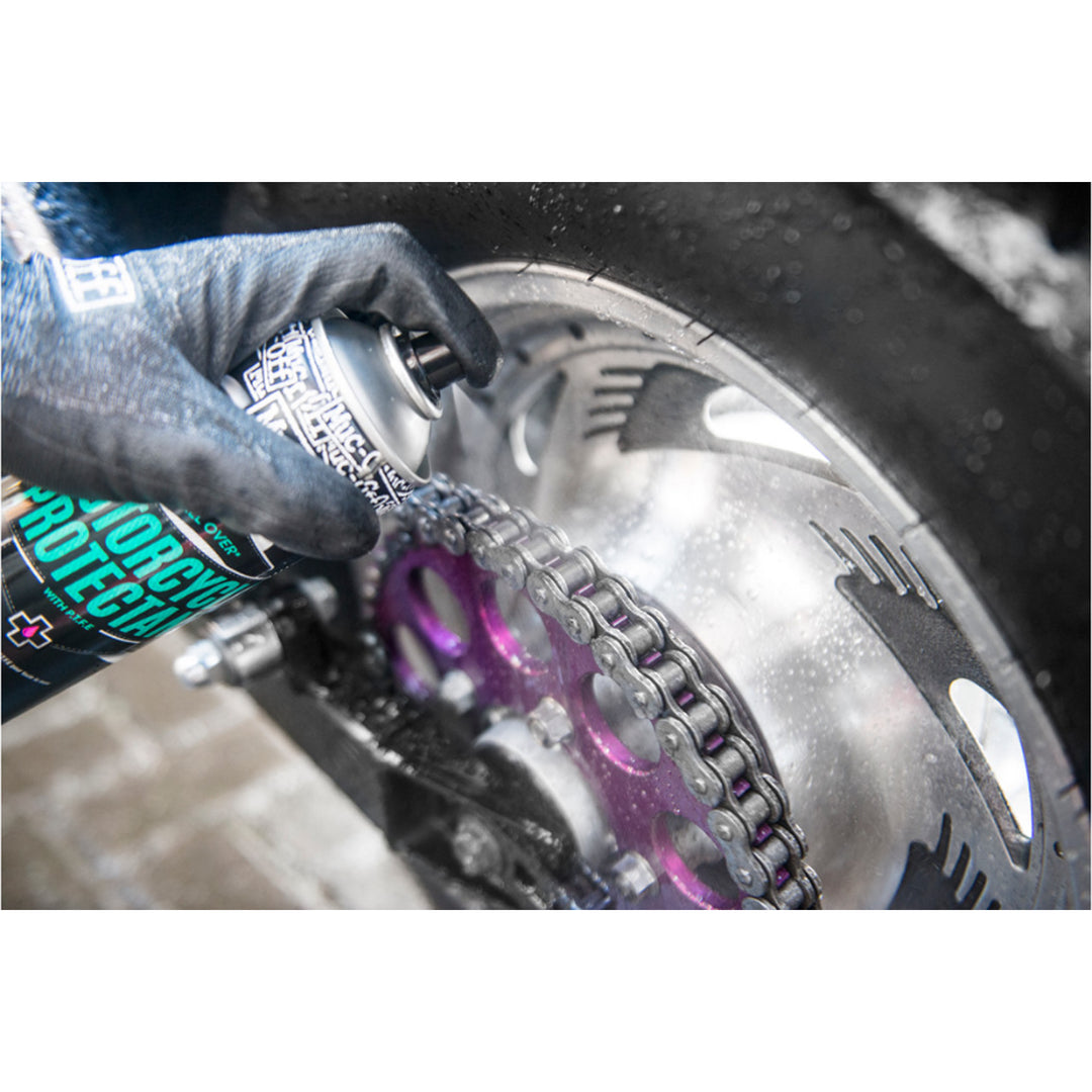 Muc-Off Motorcycle Protectant 500ml - Lifestyle Close-Up of Model Spraying Protectant on Motorcycle Chain