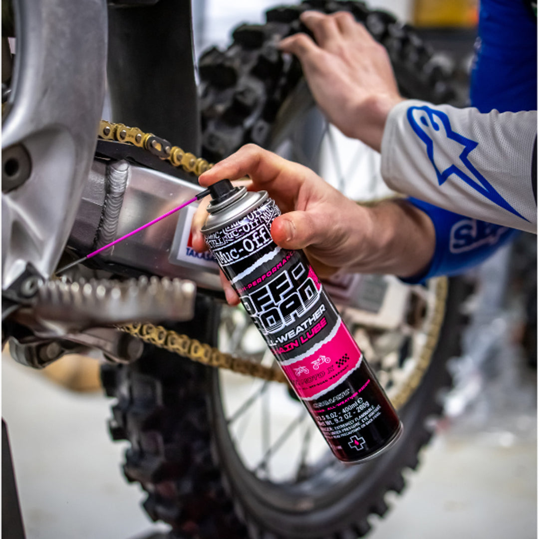 Muc-Off Offroad All-Weather Chain Lube - 400ml - Lifestyle Close-Up of Model Spraying Chain Lube on Dirt Bike Chain