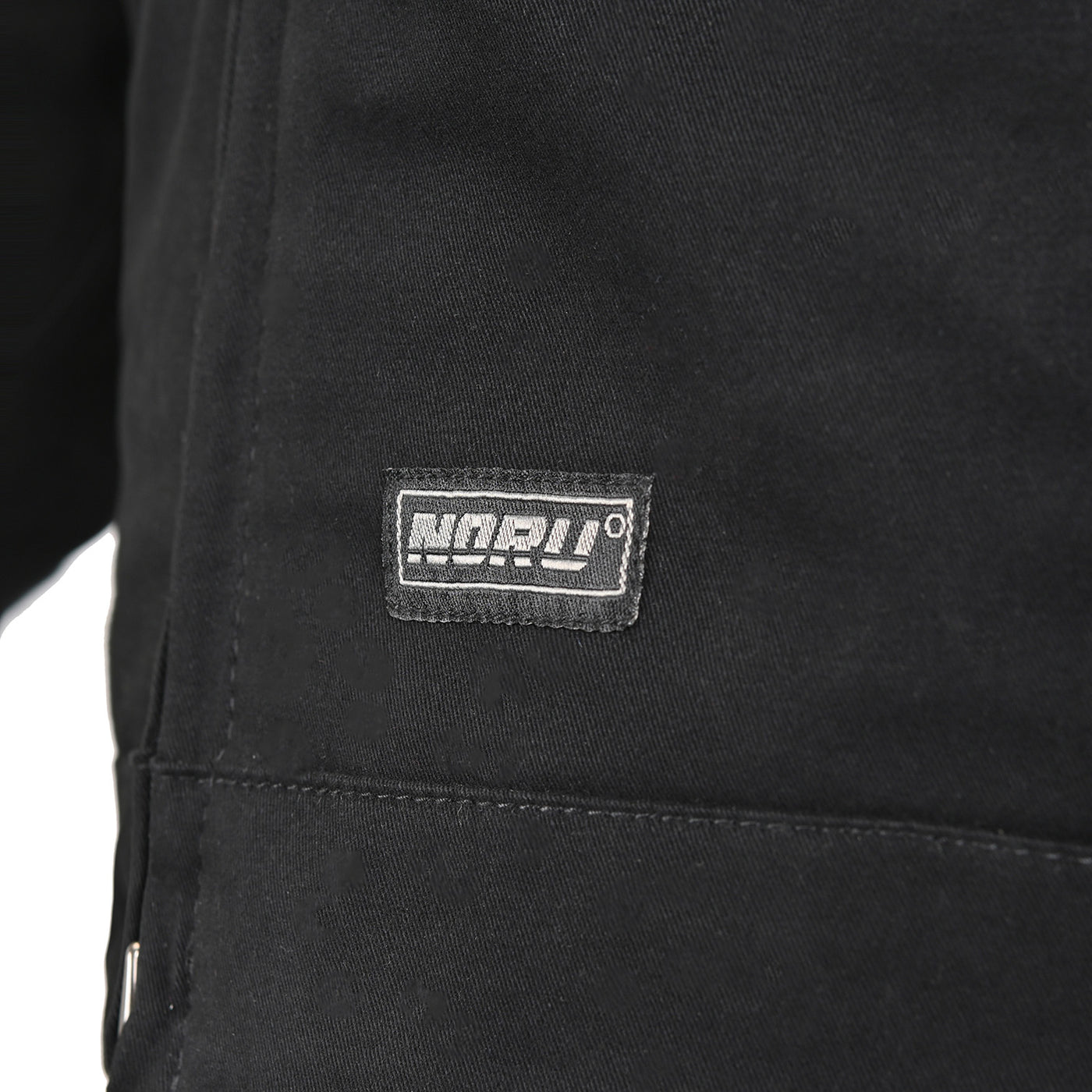 Noru Spanner Jacket Black - Close-Up of Brand Logo Tag on Lower Front
