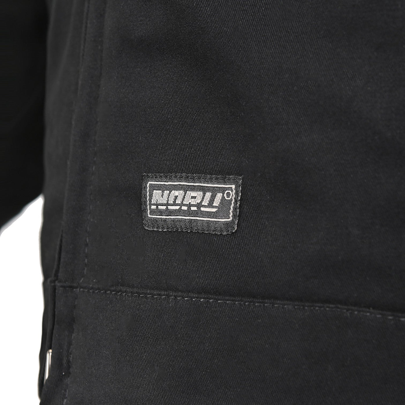 Noru Spanner Jacket Black - Close-Up of Brand Logo Tag on Lower Front