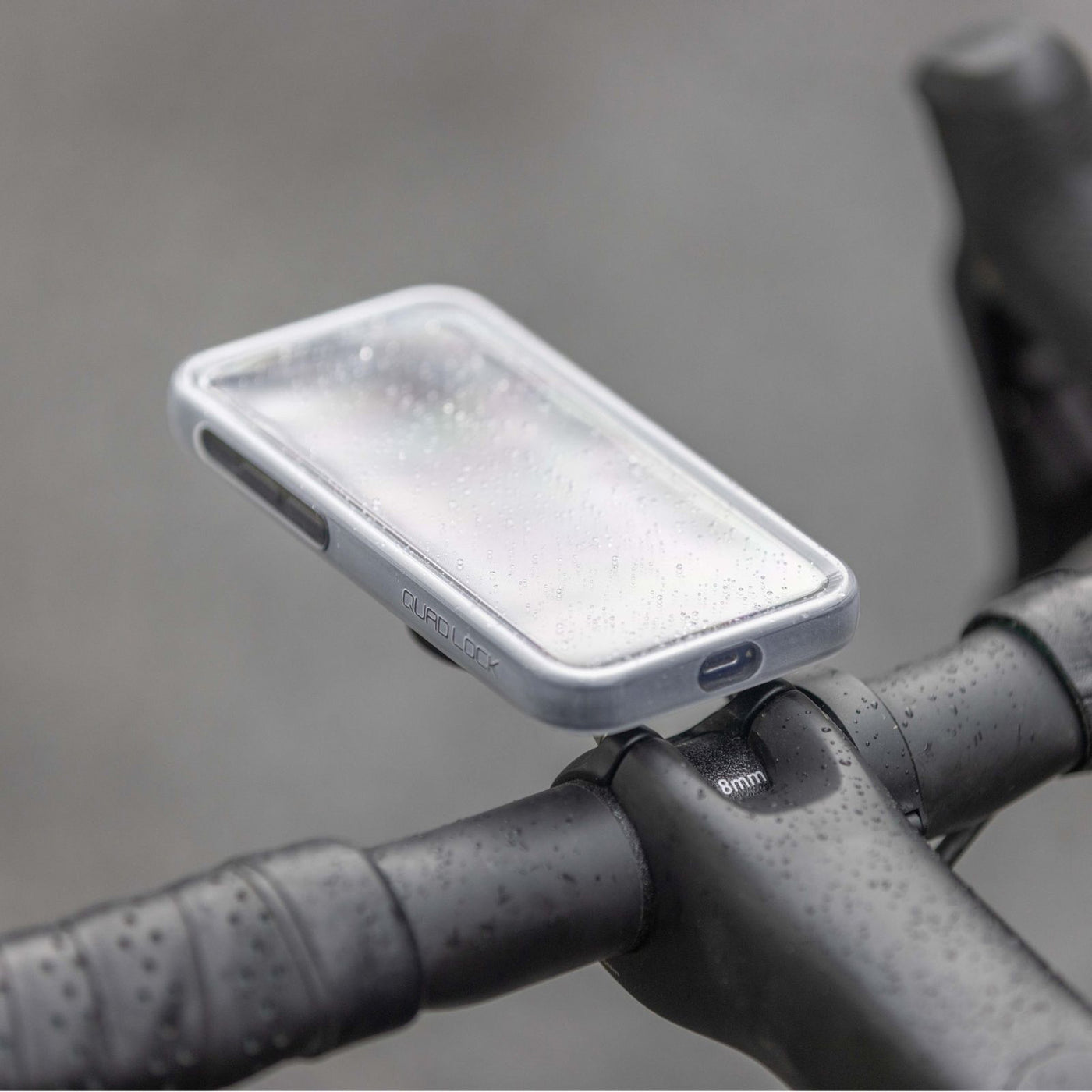 Quad Lock Phone Poncho - iPhone 16 Series - Lifestyle Shot of Bicycle Handlebar Set-Up in Rain