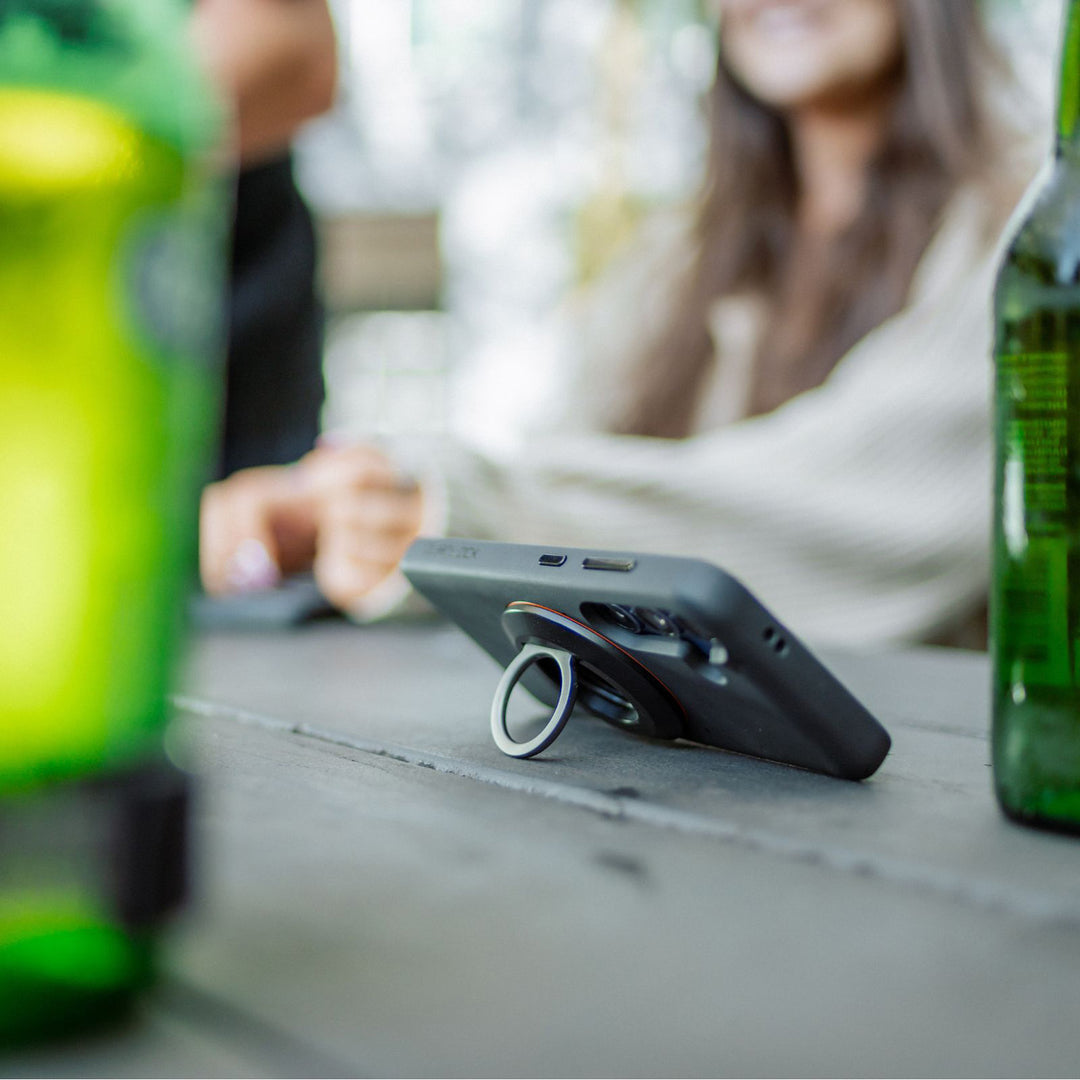 Quad Lock MAG Phone Ring Grip/Stand/Bottle Opener - Lifestyle of Ring Stand Propping Up Phone on Picnic Table