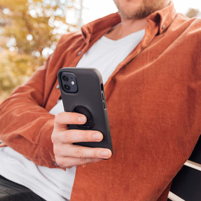 Quad Lock Phone Case - iPhone 12 Series MAG - Lifestyle Shot of phone case held in hand of model sitting on bench