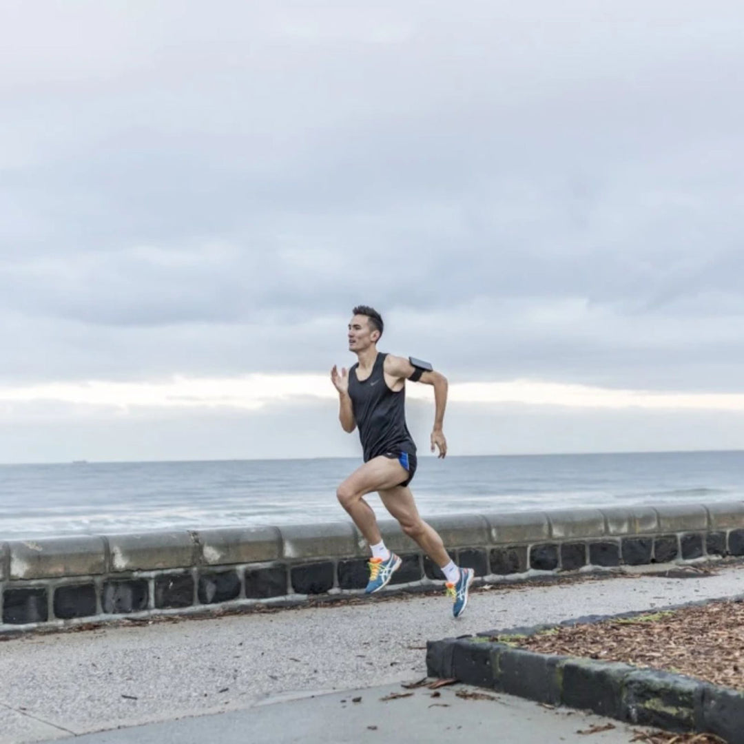 Quad Lock Sports Armband - Lifestyle Wide Shot of Jogger Running Along Beach  with Phone on Armband