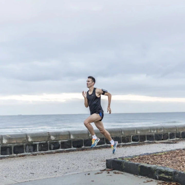 Quad Lock Sports Armband - Lifestyle Wide Shot of Jogger Running Along Beach  with Phone on Armband