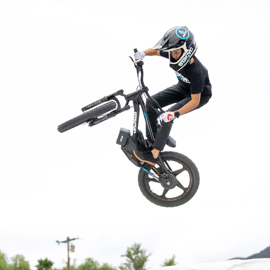 Stacyc Electric Bikes Stacyc 20EDRIVE - Lifestyle Undershot of Youth Rider on Stacyc 20EDRIVE Performing Trick in the Air Against Bright Sky Background