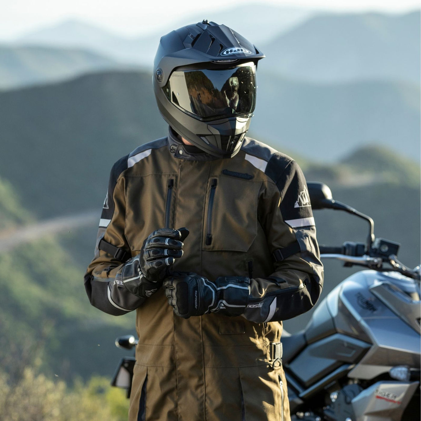 Tourmaster Centurion Laminated 1-Piece Suit Gun/Sand - Lifestyle of Rider standing in front of gray motorcycle