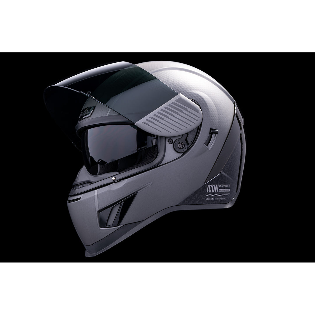 ICON Airform™ Counterstrike MIPS® Helmet Silver - Front Left Side View with Dark Studio Background, Faceshield Raised, and Drop Down Sun Visor Lowered