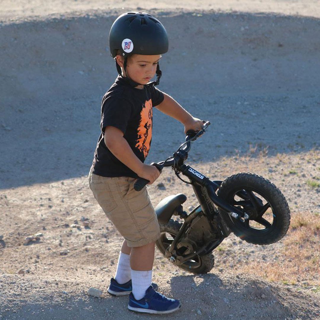 Stacyc Electric Bikes Stacyc 12EDRIVE - Lifestyle of Toddler Lifting Bike over Dirt Mound