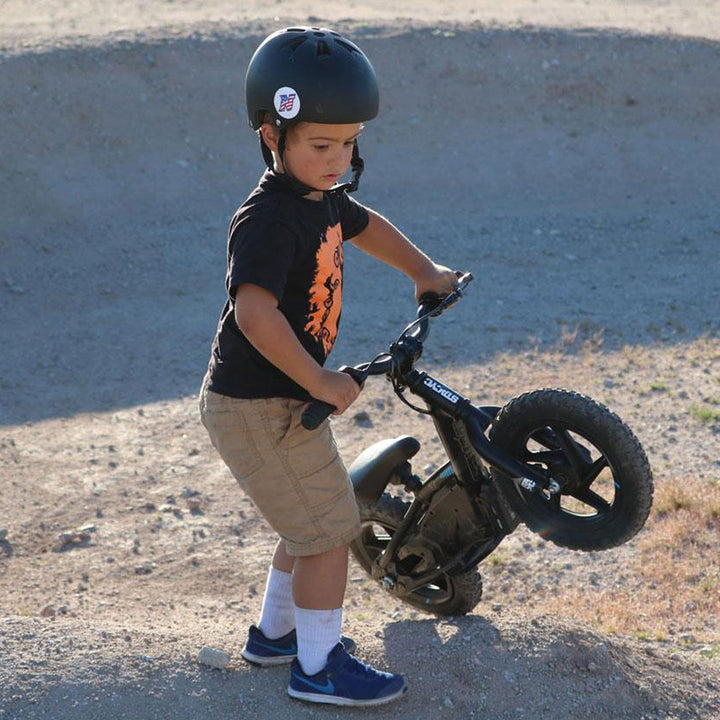 Stacyc Electric Bikes Stacyc 12EDRIVE - Lifestyle of Toddler Lifting Bike over Dirt Mound