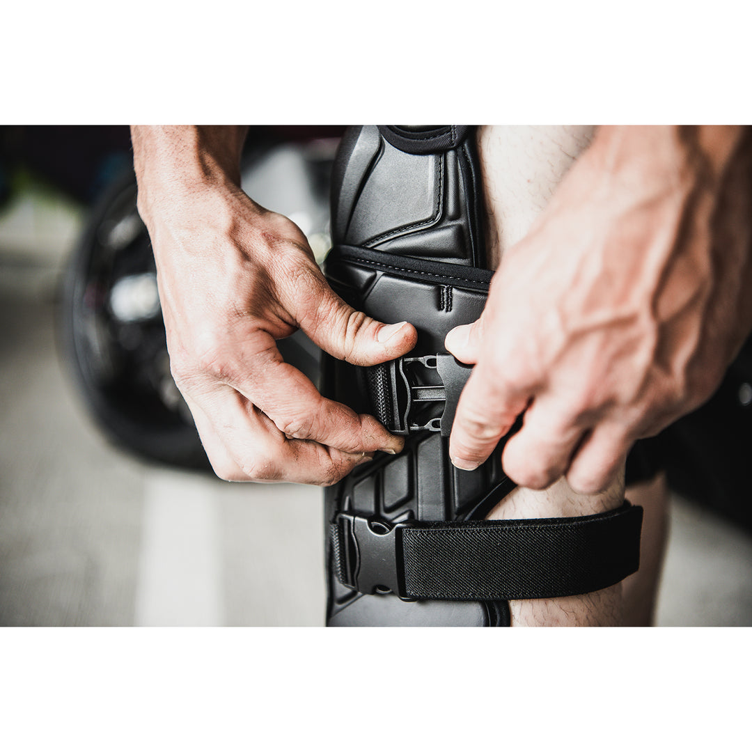ICON Field Armor 3™ Knees Black - Lifestyle Close-Up of Rider Strapping on Knee Armor
